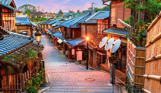 Traditional Japanese village street with wooden buildings, blue tile roofs, and lantern lighting at dusk